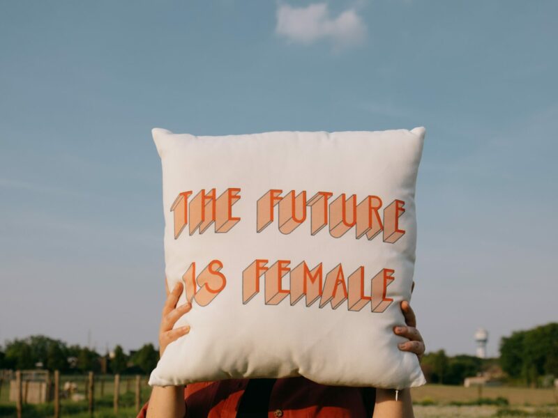 Woman stands in a field holding a pillow that says the future is female