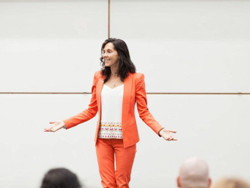 Penny Tremblay wears a coral suit while speaking to a group