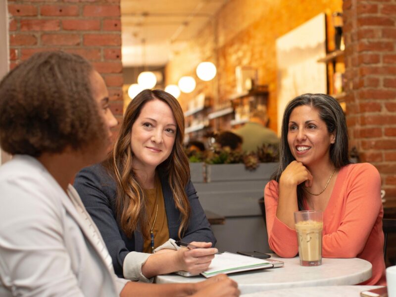 Three women sit at a table having a friendly and professional discussion